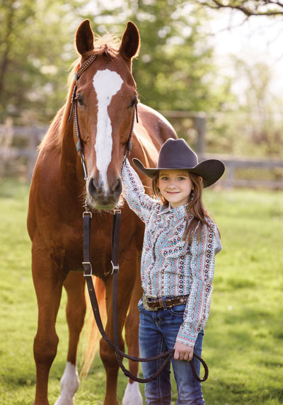 A young girl in a cowboy hat standing with her horse